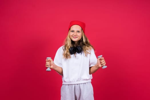 Kid girl doing fitness exercises with dumbbells on a red background