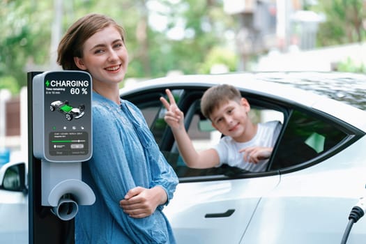 Environmental awareness family with eco-friendly electric car recharging battery from home EV charging station with little boy inside the car. Rechargeable and EV car technology. Perpetual