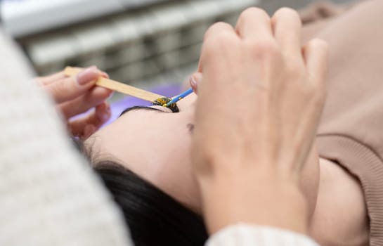 Beauty concept. Eyelash extensions. A beautiful girl lies on a couch in a beauty salon. The master does eyelash extensions. Close-up.