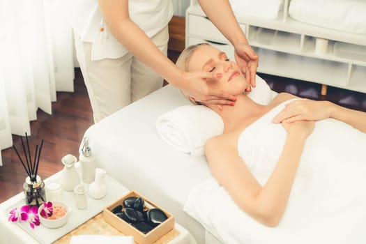 Caucasian woman enjoying relaxing anti-stress head massage and pampering facial beauty skin recreation leisure in dayspa modern light ambient at luxury resort or hotel spa salon. Quiescent