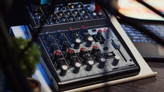 Close up shot of professional analog mixer with mixing channels, onboard effects and quality microphone able to produce impeccable sound during podcast recording in dimly lit studio