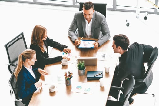 Businessman executive in group meeting discussion with other businessmen and businesswomen in modern office with coffee cups and documents on table. People corporate business working team concept. uds