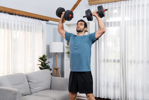 Athletic body and active sporty man lifting dumbbell weight for effective targeting muscle gain at gaiety home as concept of healthy fit body home workout lifestyle.