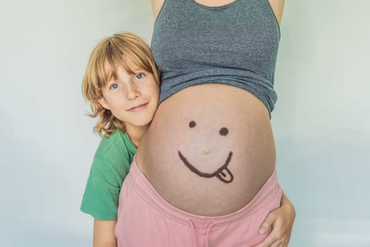 Adorable moment as a son adds a touch of joy to his mother's pregnancy, playfully drawing a funny face on her baby bump, creating cherished memories.