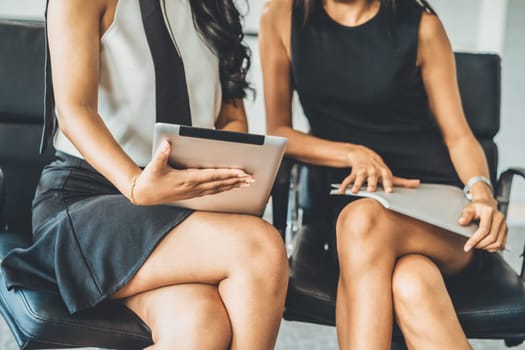 Two businesswomen discussing business while looking at financial data in their hands. They are sitting on the chairs in the office meeting room. uds