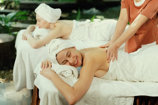 A portrait of two young attractive woman lie on bed during having back massage by a professional masseur at outdoor surrounded by peaceful natural environment. Healthy and beauty concept. Tranquility.