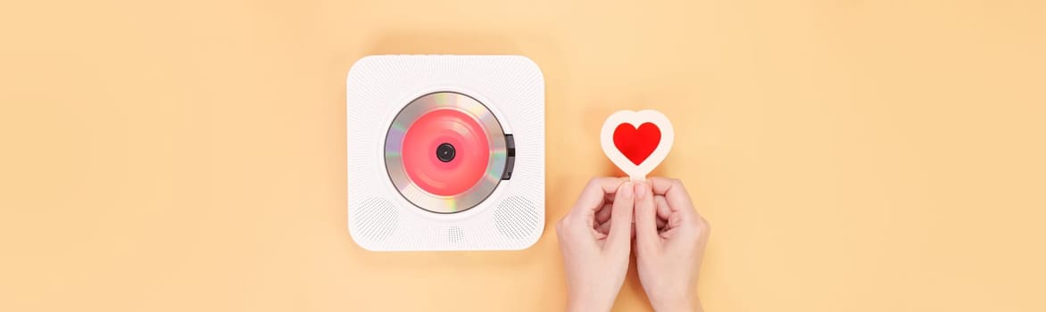 Hands holding heart shape red gift card next to white cd player with red disc on yellow background. Love music, Valentine day, Greeting, retro Love song, space for text