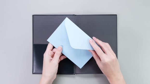 Blue mockup envelop with empty space for text and design in hand of young woman on grey background. Board, blank, template, mockup, gift, book, greeting card, layout for a slogan