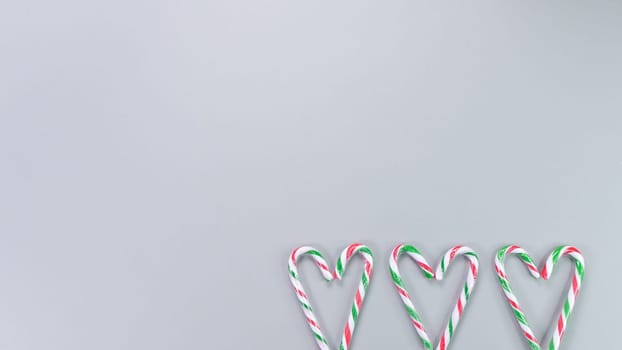 Red, green and white candy canes in the shape of heart on grey background. Valentine's Day concept. Greeting card with copy space for your text or advertising, flat lay