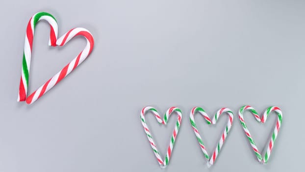 Red, green and white candy canes in the shape of heart on grey background. Valentine's Day concept. Greeting card with copy space for your text or advertising, flat lay