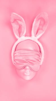 Pink sleeping eye mask on mannequin face with fluffy Easter bunny ears. Image is toned in Viva Magenta color of year 2023. sleeping disorder. Holidays, Head accessory. Plastic face
