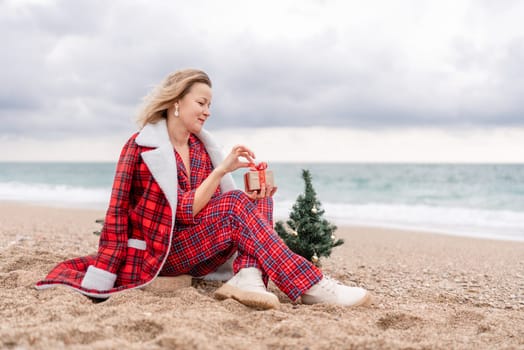 Lady in plaid shirt holding a gift in his hands enjoys beach with Christmas tree. Coastal area. Christmas, New Year holidays concep.