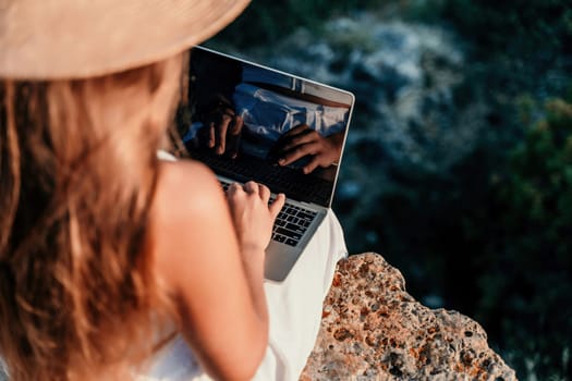 Freelance women sea working on the computer. Good looking middle aged woman typing on a laptop keyboard outdoors with a beautiful sea view. The concept of remote work