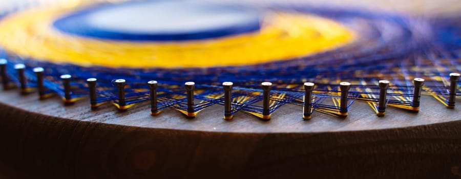 Colored thread mandala on a wooden board with nails. Mandala Moon Harmony Sun esotericism and psychology pictures from yellow and blue silk threads