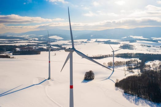 Wind turbines that produce electricity in the winter field at sunset.