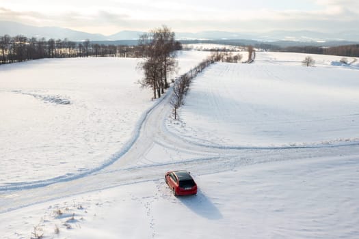 Red Car Driving Down Snow Covered Road, Winter Journey Through Scenic Landscape.