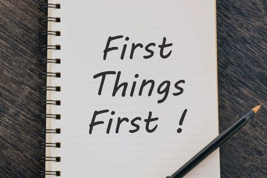 First Things First text on notepad with pen on wooden desk.