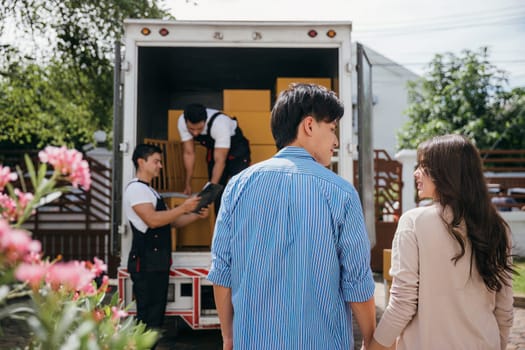 With professional help a couple moves into their new house smoothly. The delivery team collaborates unloading and lifting cardboard boxes for an efficient relocation. Moving Day Concept