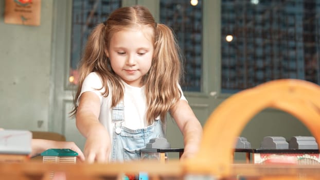 Multicultural girl playing toy to improve and develop creativity. Diverse student sitting while holding car model at playroom in elementary school at break time. Creative activity concept. Erudition.