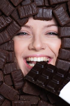 The face of a caucasian woman surrounded by chocolates. The girl eats a bar of chocolate