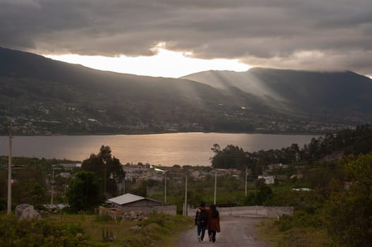 A pair of individuals walking together on a dirt road in Ecuador, surrounded by scenic landscapes.