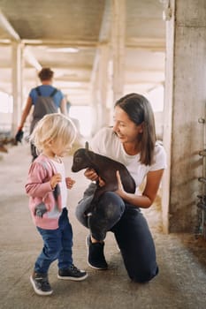 Smiling mother showing little girl a brown goatling in her arms. High quality photo