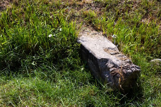 Concrete Pillars Lying On The Ground With Grass Growing And Dead Leaves. One large piece of an old concrete post lies on the grass in the garden.

