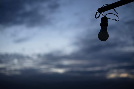 An image of an unlit light bulb against a  cloudy sky.