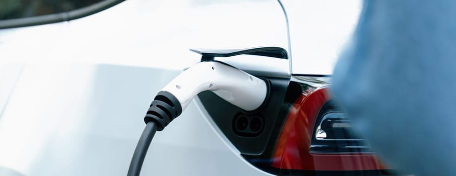 Panorama closeup EV charger handle plugged in or connect to electric car, recharging EV car battery with alternative and sustainable energy with zero CO2 emission for clean environment. Perpetual