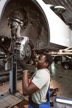 African male auto-mechanic repairing car brakes under the car in auto service close up