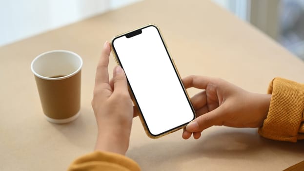 Closeup young woman holding mobile phone on working desk with paper cup of coffee.