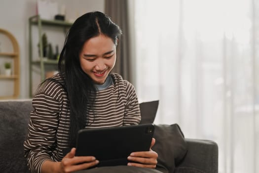 Carefree young woman browsing internet or watching video on digital tablet at home.