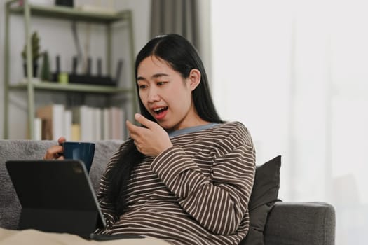 Surprised young woman covering opened mouth reading unbelievable good news on digital tablet.