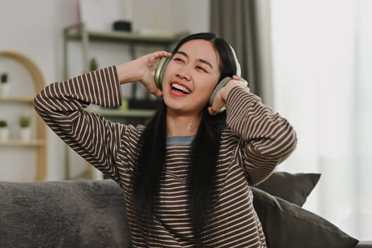 Cheerful asian woman wearing headphones and singing her favorite song at home.