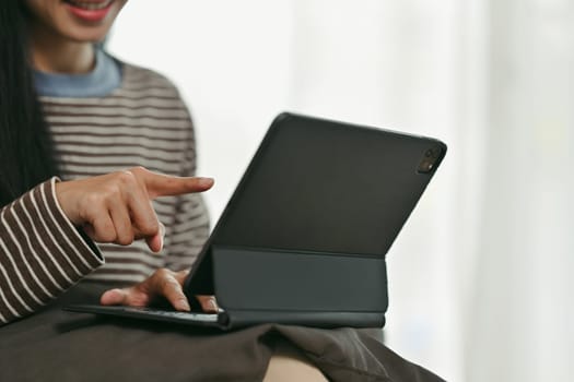 Smiling young woman pointing at digital tablet screen browsing internet or working online at home.