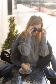 Young woman enjoying a coffee, sitting with mobile phone on the cafe terrace on the old city street during a sunny day. High quality photo