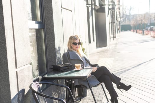 Young caucasian woman business woman drinks coffee at coffee shop terrace. High quality photo