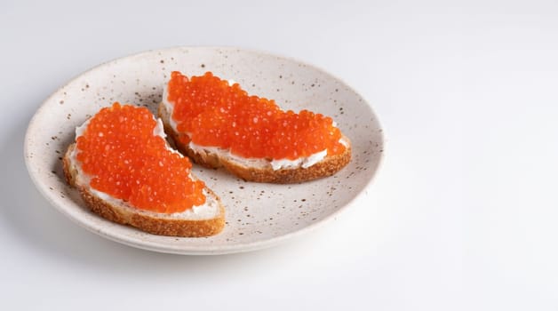 Two sandwiches with red caviar on a plate. A delicious appetizer of trout caviar on a slice of bread with cream cheese. Salted salmon caviar for fish delicacy concept.