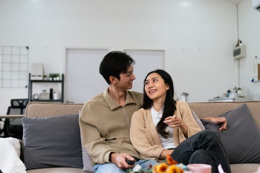 Couple Watches TV together while Sitting on a Couch in the Living Room. Girlfriend and Boyfriend embrace, cuddle, talk, smile and watch Television Streaming Services.