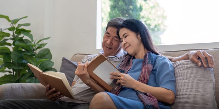 Happy elderly couple relax on couch in living room reading together for vacation holiday at home.