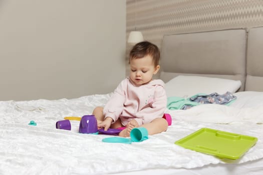 happy cute little child girl playing and pretending drinking tea from toy cups on bed