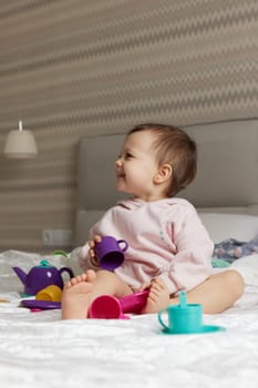 happy cute little child girl playing and pretending drinking tea from toy cups on bed