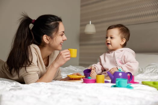 mother and little child daughter playing tea party and spending time together in bedroom, family having fun