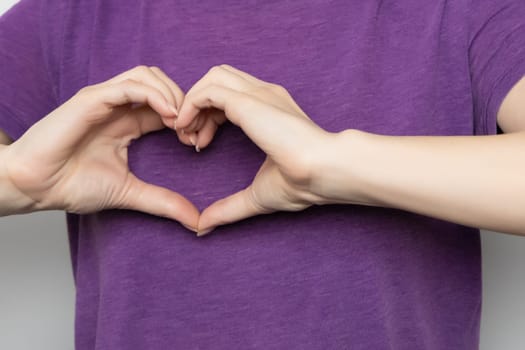 Inspire inclusion. Woman holding her hands in the shape of a heart and holding them in front of her, dressed purple t-shirt. International women's day concept