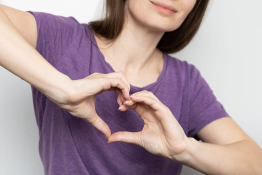 Inspire inclusion. Woman holding her hands in the shape of a heart and holding them in front of her, dressed purple t-shirt. International women's day concept