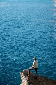 Young man stands on a stone ledge above the sea and looks into the distance. Back view. High quality photo