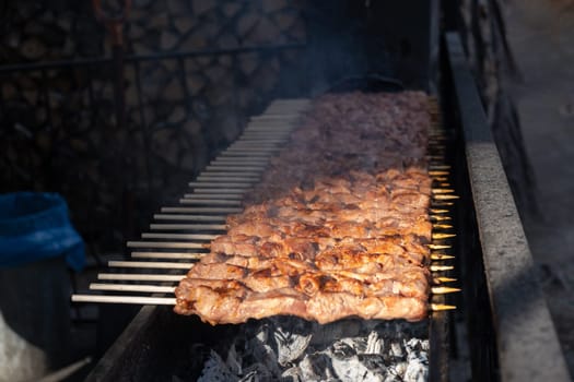 A lot of juicy meat kebabs in a row on the grill. Meat pieces strung on wooden skewers on the grill. The process of cooking kebabs with a lot of smoke. Cooking in nature