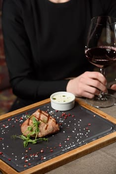 woman sitting at a table in a restaurant. He is holding a glass of red wine and eating a steak.