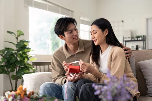 Romantic young asian couple embracing giving present in living room at home. Fall in love. Valentine concept.