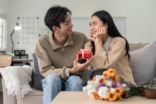 Romantic young asian couple embracing giving present in living room at home. Fall in love. Valentine concept.